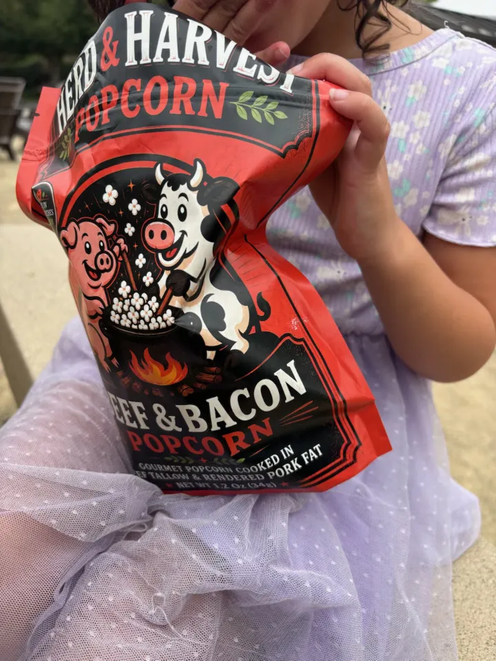 Girl holding Herd & Harvest Beef & Bacon Popcorn bag — cooked in beef tallow and rendered pork fat